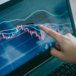 Hand pointing at stock market graph on laptop screen
