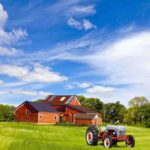 A vintage tractor in front of a red barn on a sunny day