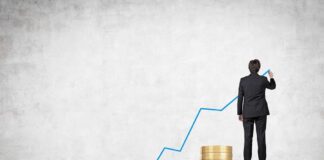 Businessman standing on stacks of coins drawing a growth chart