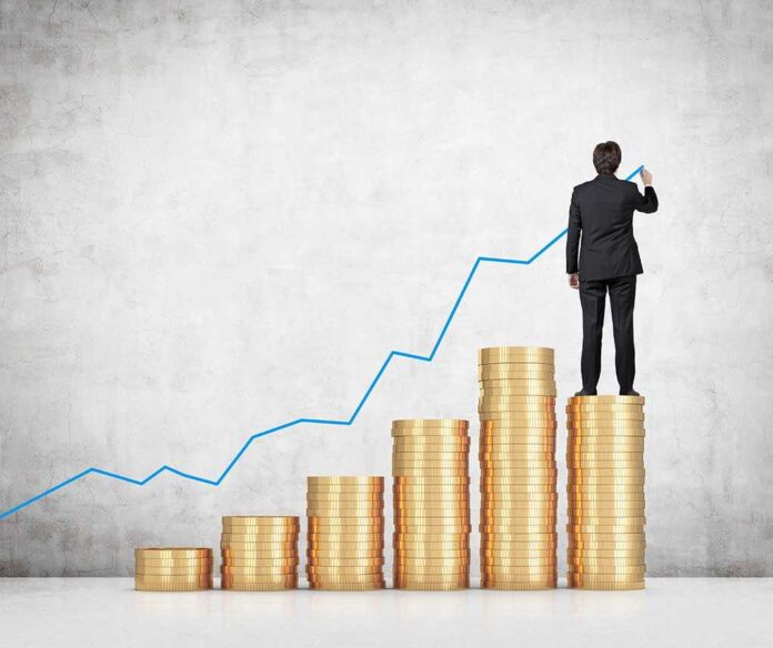 Businessman standing on stacks of coins drawing a growth chart