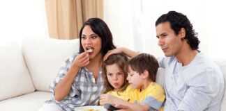 A family of four enjoying a movie night on the couch with snacks