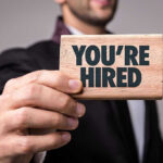 Public University’s OUTRAGEOUS Anti-American Hiring Scandal Person holding a Youre Hired sign.