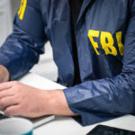 Person in FBI jacket typing on a laptop.