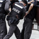 Meth-Crazed Driver Hijacks Patrol Car Police officers arresting a handcuffed person.