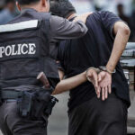 19 Rescued in Holiday Trafficking Sting Police officer arrests handcuffed person.
