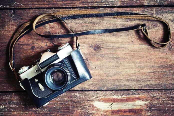 A vintage camera resting on a wooden surface with a leather strap