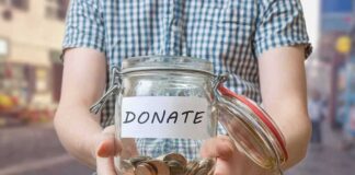 Person holding a glass jar labeled 'DONATE' filled with coins