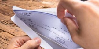 A hand holding an envelope containing a check on a wooden table