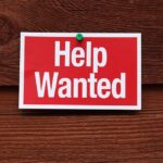 Unprecedented Jobs Boom Shocks Experts A red and white Help Wanted sign pinned to a wooden surface