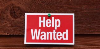 A red and white Help Wanted sign pinned to a wooden surface
