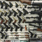 Historic Crime Plummet — But Gun Debate Rages On Wall display with handguns and rifles for sale.