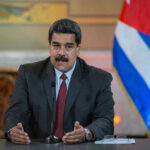 Manhattan Indictment Unveils Maduro’s Drug Empire Man speaking at podium with Cuban flag in background.