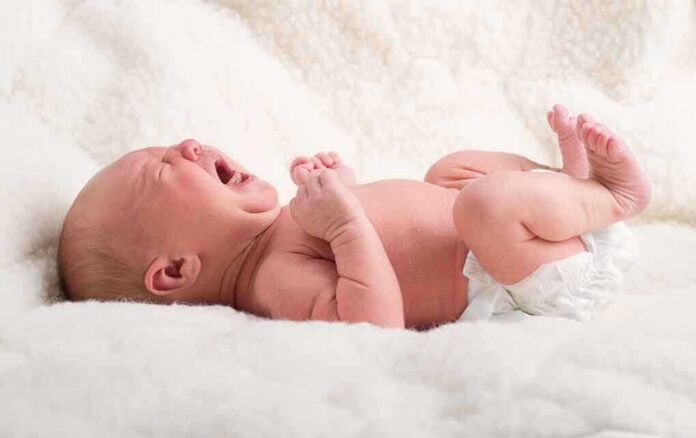 A newborn baby lying on a soft blanket, crying with a distressed expression