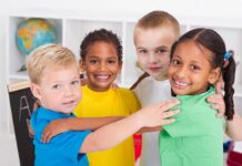Four children of diverse backgrounds smiling and hugging each other in a classroom