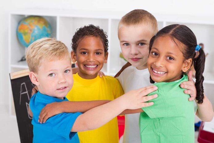 Four children of diverse backgrounds smiling and hugging each other in a classroom