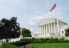 The U.S. Supreme Court building with an American flag and landscaped grounds