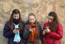 Three teenagers using smartphones while standing against a textured wall