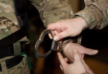 A military personnel placing handcuffs on an individual