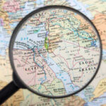 Magnifying glass over Middle East map highlighting Israel and Egypt.