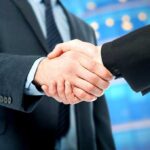 Tea Time with King Charles: What’s Really at Stake? Two business professionals shaking hands in a corporate setting