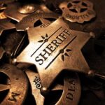 A collection of vintage sheriff badges arranged on a dark surface