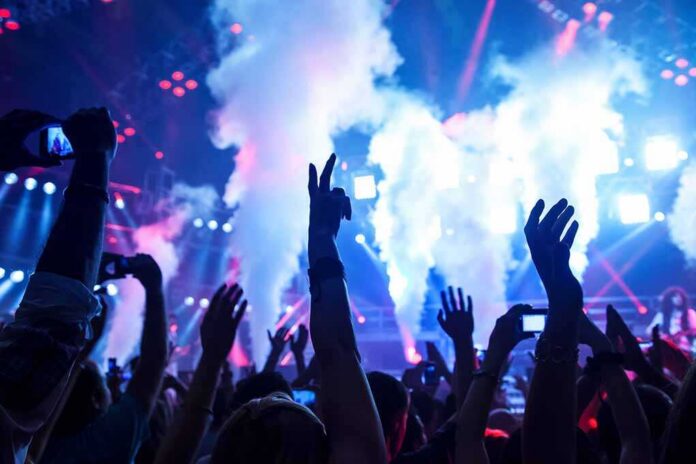 Crowd at a concert with hands raised and smoke effects in the background