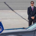 A security officer in a suit stands guard near a presidential vehicle at an airport