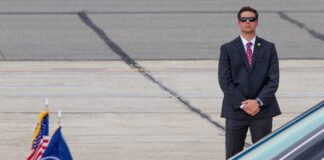 A security officer in a suit stands guard near a presidential vehicle at an airport
