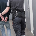 Officer escorting handcuffed person down hallway.