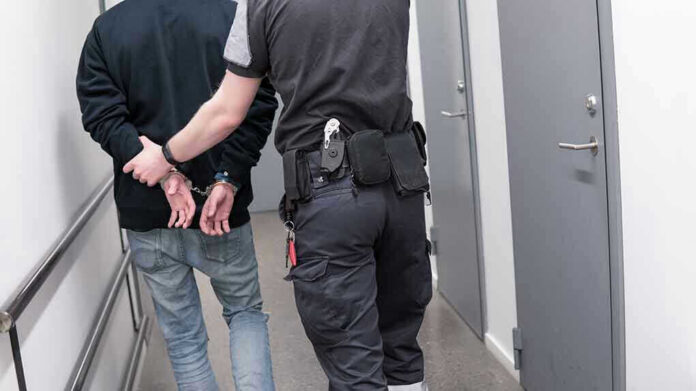 Officer escorting handcuffed person down hallway.