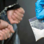 Person handcuffed, police holding bag of white substance.