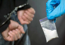 Person handcuffed, police holding bag of white substance.