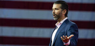 Man speaking in front of American flag backdrop.