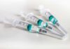 Three syringes filled with blue-green liquid on a white surface