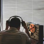 Person wearing headphones listening to a reel-to-reel tape recorder