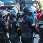 Riot police in helmets and visors stand in a line