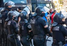 Riot police in helmets and visors stand in a line