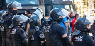 Riot police in helmets and visors stand in a line