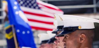 U.S. Marines in uniform standing in formation with flags in the background