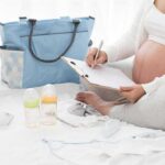 Pregnant woman writing a checklist beside a baby bag