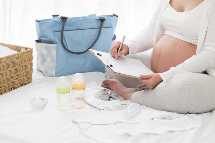 Pregnant woman writing a checklist beside a baby bag