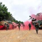 Soldiers running with armored vehicles through red smoke