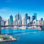 Brooklyn Bridge spanning blue river with modern city skyline
