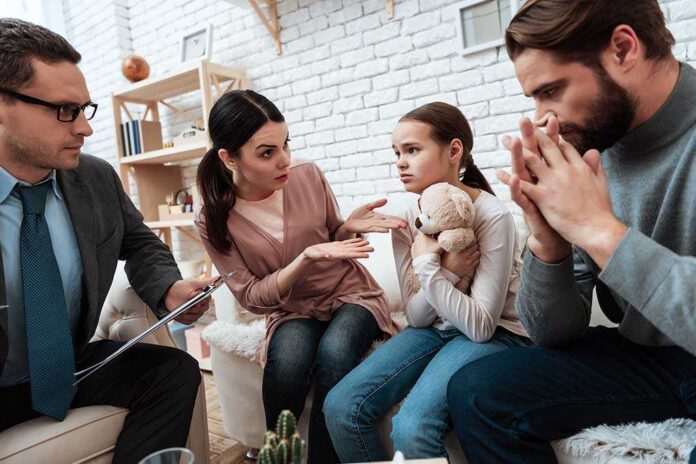 Family and counselor in tense discussion with upset child holding teddy bear