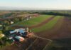 Aerial view of a farm with red barns and expansive green and brown fields