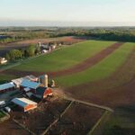 Aerial view of a farm with red barns and expansive green and brown fields