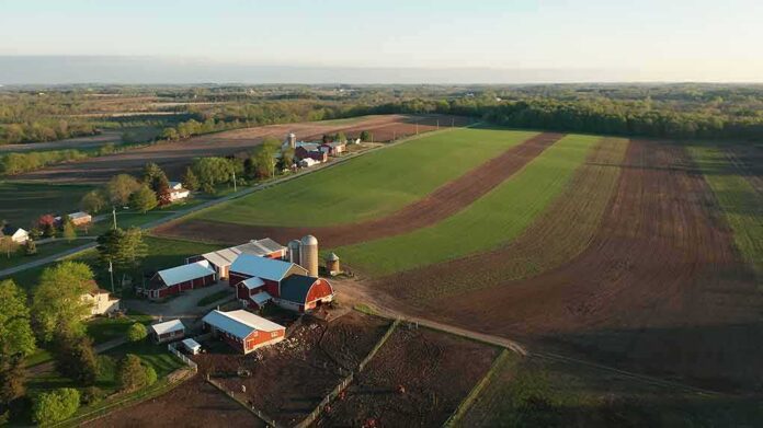 Aerial view of a farm with red barns and expansive green and brown fields