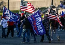 Crowd of people carrying political and American flags at a street gathering