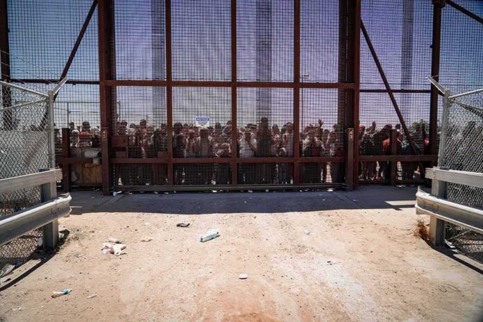 Crowd stands behind a tall metal fence at a border gate