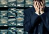 Man in suit covering face beside stacks of paperwork